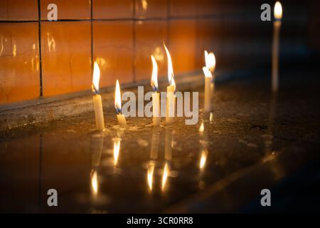 Candles burning in church interior, reflecting on wet surface. Flickering hope in dark. Silent light in still water. Prayer and worship Stock Photo