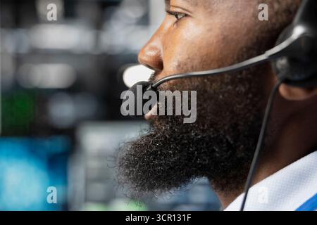 Close up of employee in server farm talking in mic, coordinating technicians. Data center support specialist supporting engineering team doing hardware maintenance, speaking in microphone Stock Photo