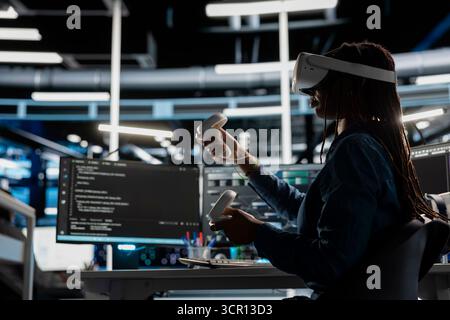 Data center engineer wearing VR equipment using artificial intelligence neural networks technology. Server farm employee using virtual reality headset and AI programming language to configure hardware Stock Photo