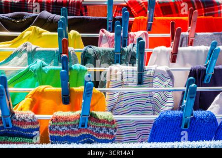 Multi-colored clothes hang attached to clothespins and dry after washing, close-up. Stock Photo