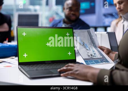Expert works on plant modernization plans using mockup notebook. Factory manager looks over facility upgrade schematics, writing plan for operational efficiency improvements on chroma key laptop Stock Photo