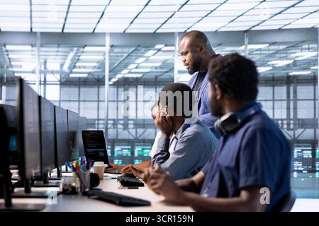 Team of data center office system administrators using programming languages to construct algorithms and build applications. African american server farm IT professionals debugging and optimizing code Stock Photo