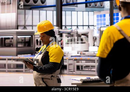 Female data scientist with tablet, working in renewable energy facility and monitoring solar panels. Factory consultant ensuring efficiency, safety and sustainability in manufacturing operations. Stock Photo
