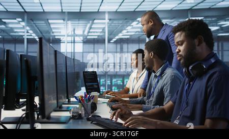 Teamworking computer scientists talking in server room, developing disaster recovery plans. Team of data center office coworkers doing brainstorming, monitoring metrics across devices Stock Photo