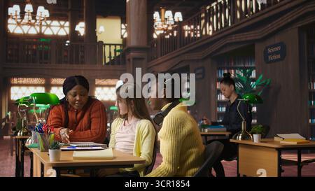 Satisfied teenagers students doing high five next to tutor in the library, feeling happy with their progress on school subjects. Professor being proud of her scholars at private lessons. Camera A. Stock Photo