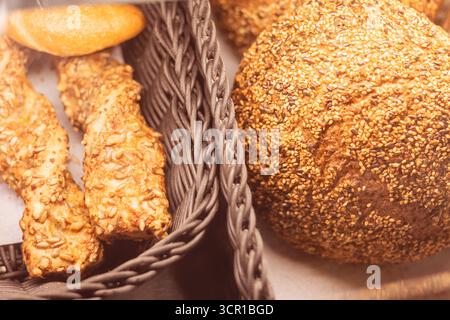 Various types of freshly baked bread and pastries sit in a wicker basket at a local bakery. Sesame seed rolls and crunchy sticks fill the cozy space i Stock Photo