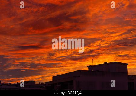 Fiery orange sunset sky with dramatic clouds over silhouetted houses, creating a vibrant evening cityscape in Algarve, Portugal. Stock Photo