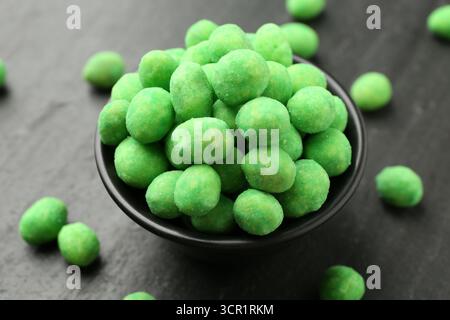 Delicious wasabi coated peanuts and bowl on dark textured table, closeup Stock Photo