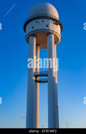 Radar tower of historic Tempelhof Airport in Berlin glowing in warm golden light against clear blue sky during early evening. Stock Photo