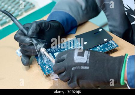 Technician performing soldering on a printed circuit board in an electronics workshop during the afternoon Stock Photo