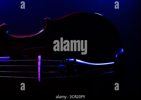 A violin on a dark background, side lit with purple and blue lights Stock Photo