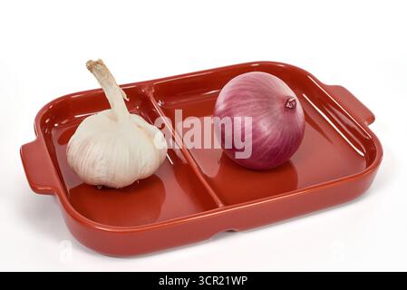 A bold still life of two essential cooking ingredients, garlic and a red onion, on a red plate. A concept for the foundation of flavor in internationa Stock Photo