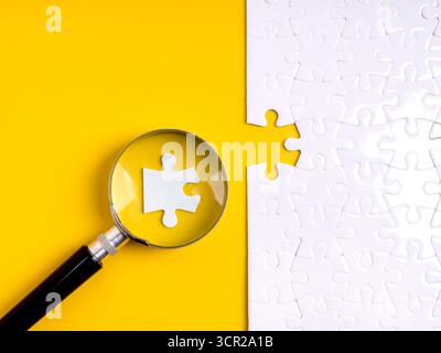 Magnifying glass focusing on puzzle piece fitting into missing part. Concept for hiring, human resource selection, recruitment, team building, employe Stock Photo