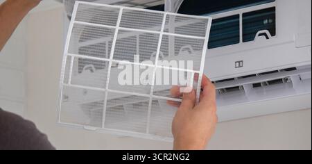 Maintenance Complete. Technician Installing Clean Air Filter in Air Conditioner. Stock Photo