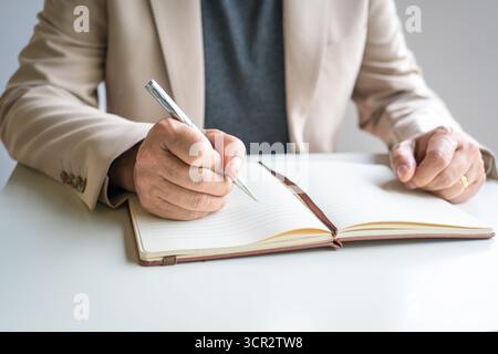 Businessman writing on notepad. Close up view of hand holding pen with notepad on desk. Stock Photo