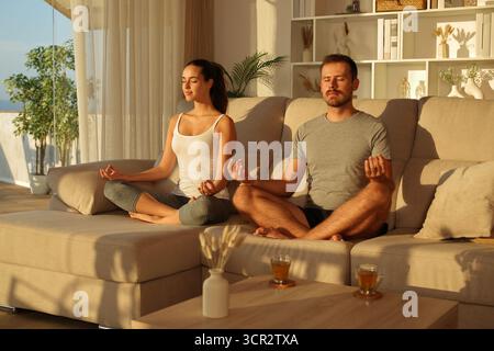 Couple of amateur yogis doing yoga exercise at home at sunset Stock Photo