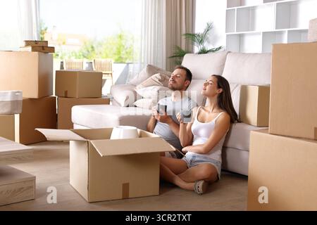 Couple moving house drinking and relaxing breathing sitting on the floor Stock Photo