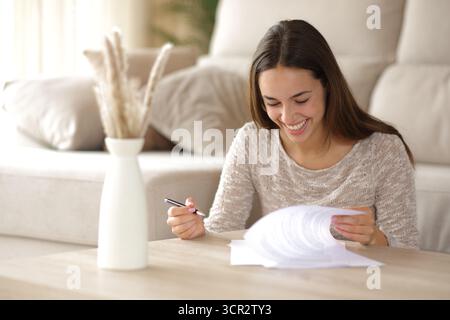 Happy woman checking paper documents to sign on coffee table at home Stock Photo