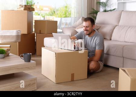 Happy homeowner moving home using laptop sitting on the floor Stock Photo