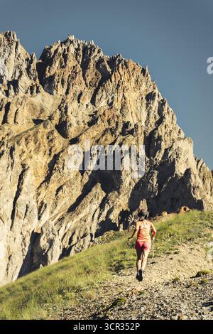 Sporty Female athlete trail runner running in motion mid air in alpine mountains, adventure fitness and endurance training in scenic landscape.Active Stock Photo
