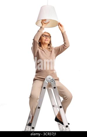 Woman on a ladder changing a pendant light bulb isolated on white background Stock Photo
