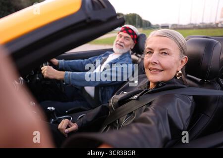 Senior woman taking selfie while man driving cabriolet outdoors, selective focus Stock Photo