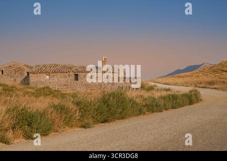 Abandoned Stone Farmhouse in Bardenas Reales Desert, Navarra, Spain. Old Rustic Structure and Dirt Road Winding Through Arid Landscape Stock Photo