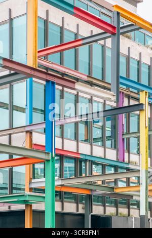 Vertical abstract shot of a colorful grid of intersecting, brightly painted steel beams contrasting with the glazed facade of a contemporary building Stock Photo