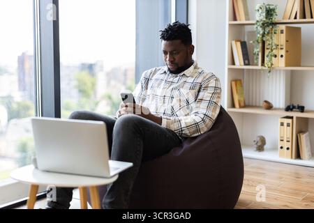 Young man seated using smartphone in modern cozy apartment interior Stock Photo