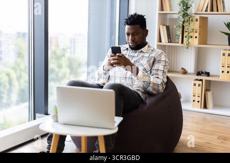 Young man seated using smartphone in modern cozy apartment interior Stock Photo