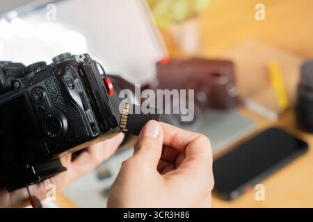 Photographer hand holds Memory card in work place. Flash card near professional DSLR camera. Close-up, selective focus. Stock Photo