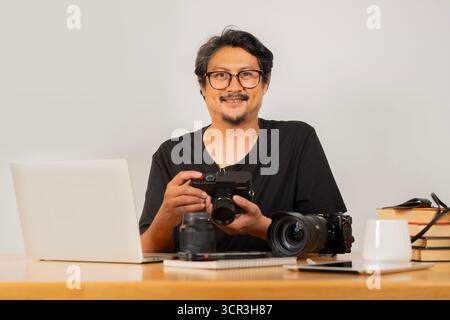 Protrait image of smiling adult handsome photographer with eyeglasses working with camera in office. Stock Photo