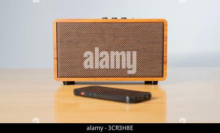 Wireless speaker connected to mobile phone - wireless mobile technology - On wooden table and white background. Selective focus. Stock Photo