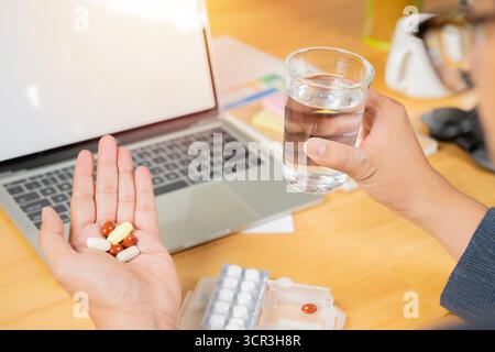 Back view and selective focus of Business man holding many pill medicine and glass of water in office. Office Syndrome concept. Stock Photo