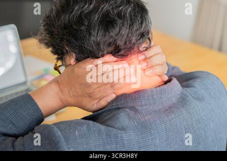 Back view of mature Asian business man in suit using computer on desk in office suffering from neck pain overworking long time to working Stock Photo