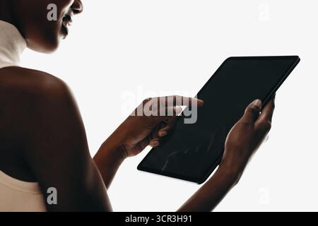 Close-up of a woman interacting with a digital tablet, cropped against a neutral setting. Ideal for themes of technology, innovation, gadgets, and use Stock Photo