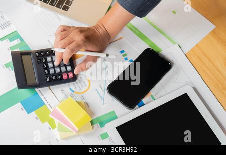 Businessman using a calculator to calculate numbers on a company's financial documents, he is analyzing historical financial data to plan how to grow Stock Photo