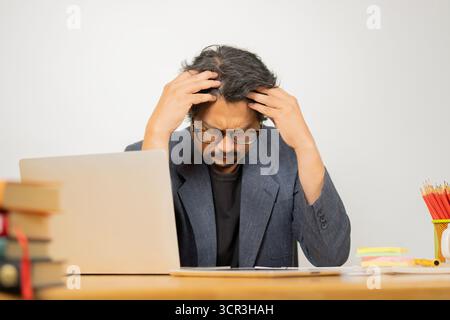 Serious frustrated businessman with closed eyes suffering from headache migraine at workplace. Stock Photo