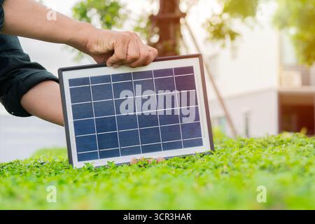 Young man hands standing in the park and holding photovoltaic mini solar panel over the bush. Concept of renewable energy, technology. Stock Photo