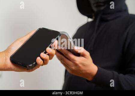 Phone in hand holding with man in black mask. Cybercrime concept. Criminal on phone, fraud, scam. Threatening call, extortion, robbery, theft, financi Stock Photo