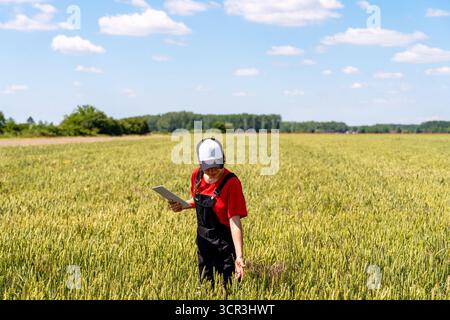Female agronomist with digital tablet checking crop growth outdoors Stock Photo