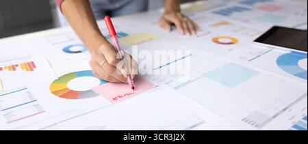 Female writes on sticky note, working in office at table Stock Photo