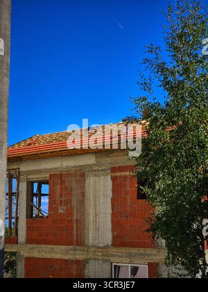 A rural house under a blue sky. An unfinished brick building. A house under construction. A house renovation. Stock Photo