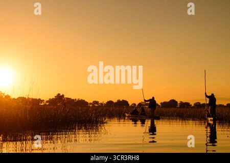 Two Makoros (also spelt mekoro, mokoro) with tourists gliding along one of the channels in the Okavango Delta at sunset. Botswana. Stock Photo