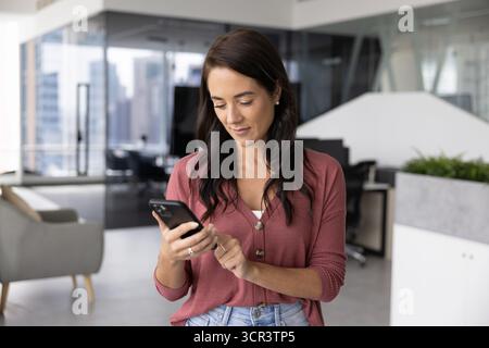 Businesslady standing in office using her smartphone Stock Photo