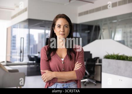Confident woman stands in modern office with arms crossed Stock Photo