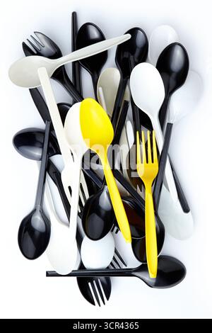 A pair of yellow plastic spoons and forks among a pile of black and white plastic spoons and forks Stock Photo