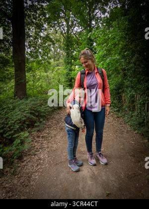 Mother and child walking on forest trail surrounded by green trees Stock Photo