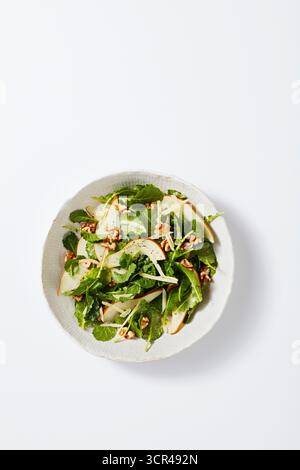 Fresh green salad with apple slices and walnuts on a white plate against a white background. Stock Photo