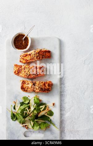 Grilled salmon fillets with herb crust served on a marble board with a side salad and dressing. Stock Photo